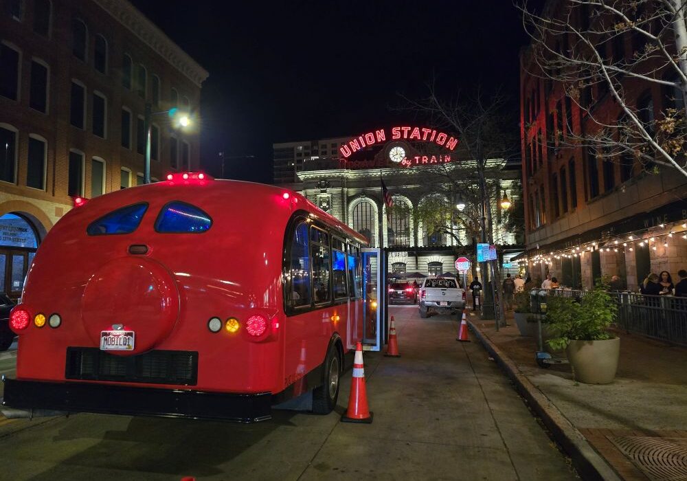 contoured red limo bus facing Denver Union Station, lit up at night