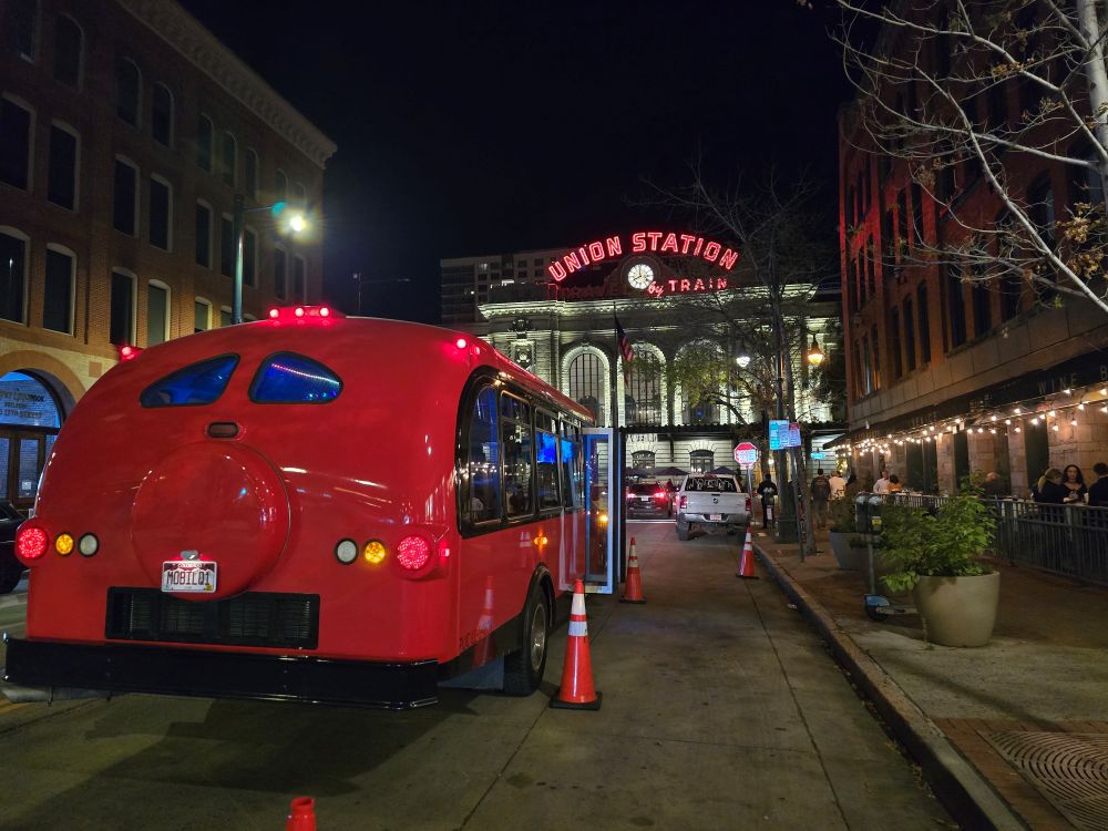 contoured red limo bus facing Denver Union Station, lit up at night