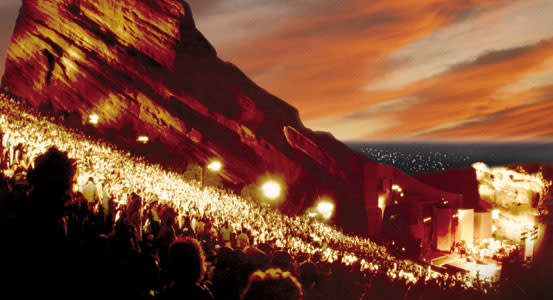 large crowd at Denver Red Rocks lit up by bright stage lights at sunset