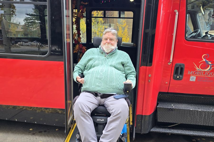 Smiling man in power wheelchair exiting a red limo party bus on a ramp
