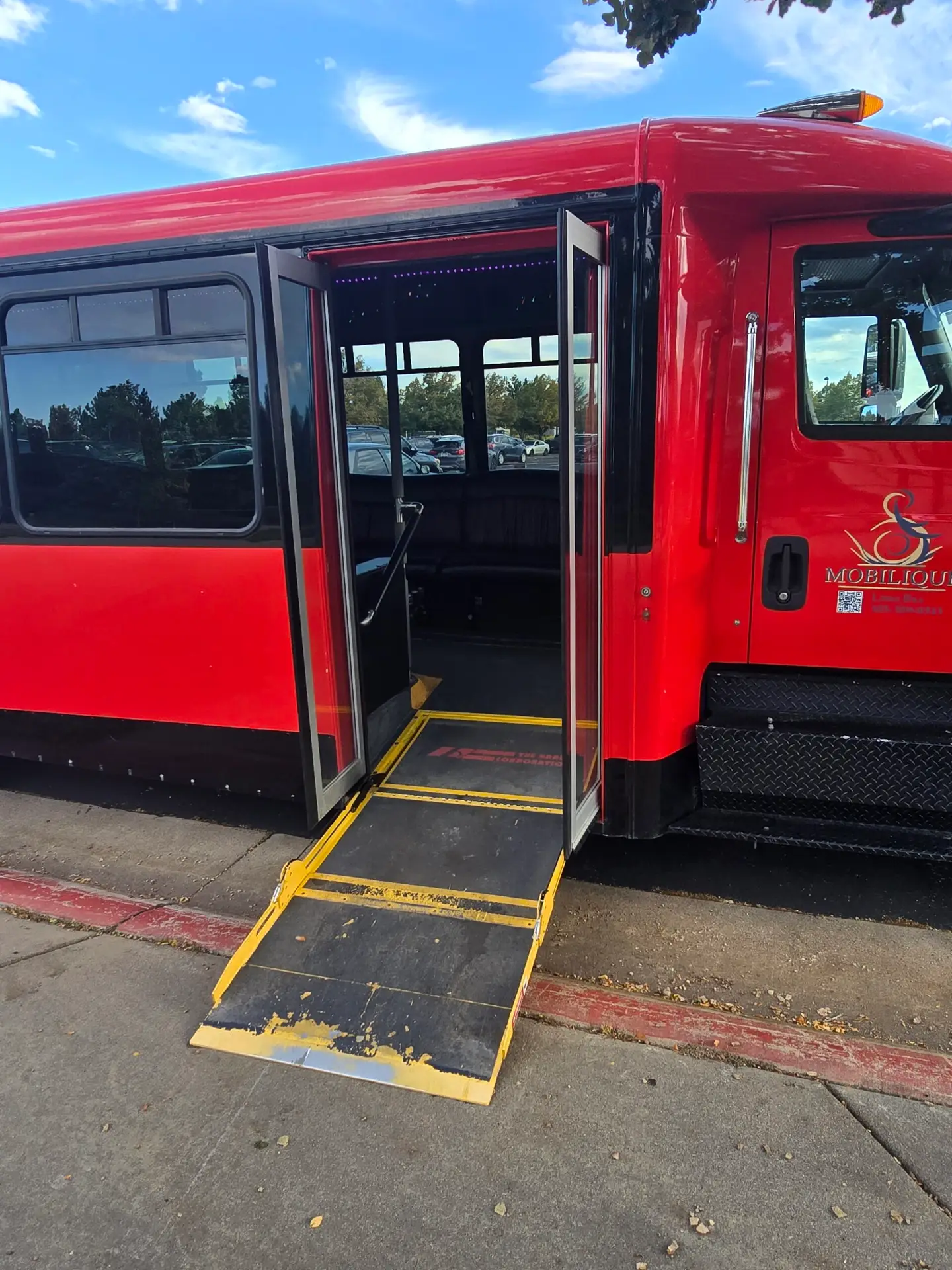 The red limo bus wheelchair ramp is fully extended onto the sidewalk