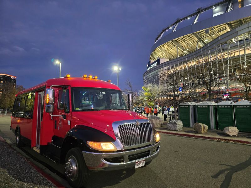 Contoured red limo bus in front of Denver Empower Field, lit up at night